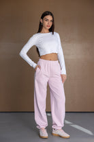 דוגמנית לובשת חולצת בטן לבנה ארוכה ומכנסי טרנינג ורודים, אופנת נשים לנוער, סטייל קז'ואל