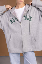 דוגמנית לובשת קפוצ׳ון אפור עם רוכסן, כיתוב NEW YORK, ג'ינס בגזרה רחבה, אופנת נשים צעירה