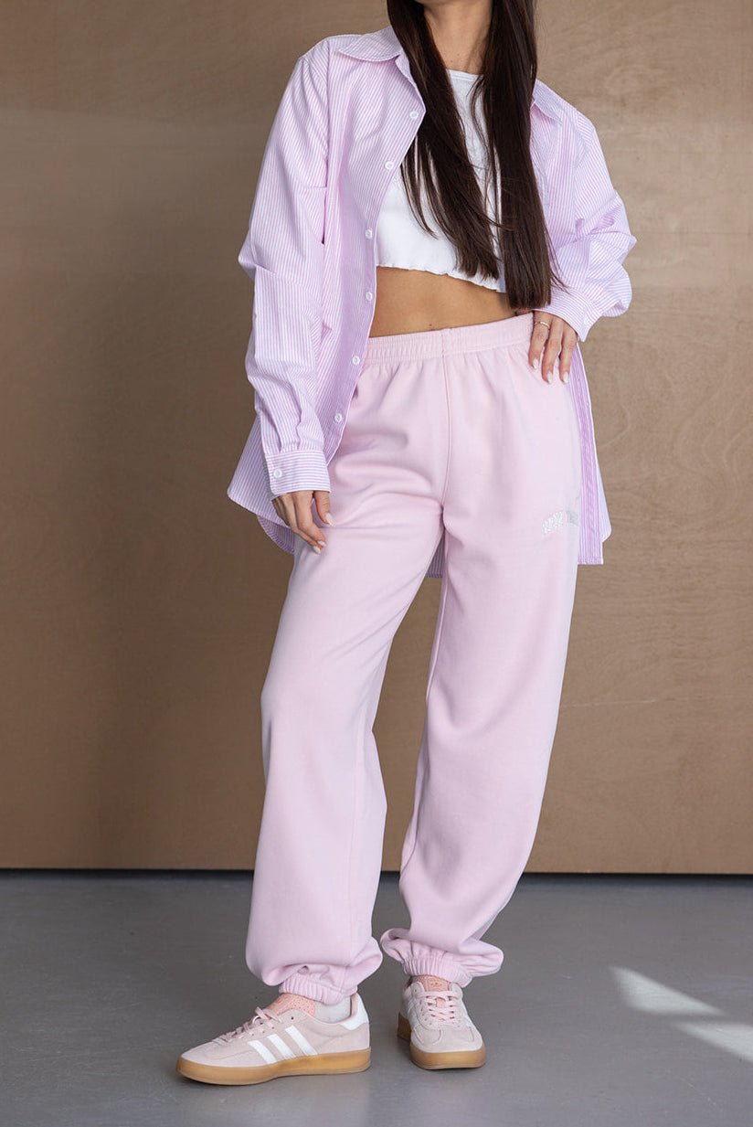 אישה לובשת מכנסי טרנינג ורודים, חולצה קצרה לבנה וחולצה מכופתרת ורודה, אופנת נשים נוחה ועדכנית