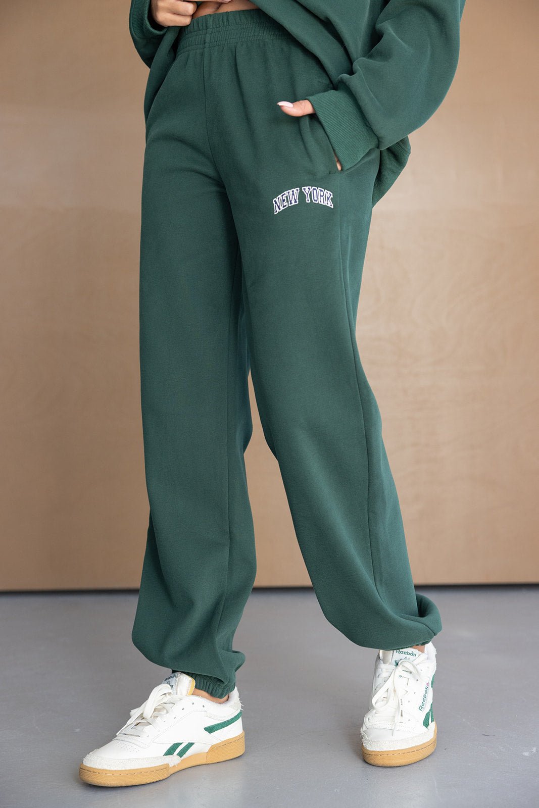 מכנסי טרנינג ירוקים לנשים עם כיתוב New York, נעלי סניקרס אופנתיות, תמונת אופנה על רקע נייטרלי