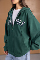 אישה לובשת סווטשירט קפוצ'ון ירוק עם ריצ'רץ' ומכנסי ג'ינס קלילים, עיצוב ניו יורק אופנתי