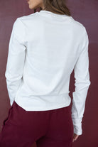 אישה לובשת חולצה לבנה ארוכה ומכנסיים בורדו, צילום גב, אופנה לנשים