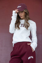 אישה לובשת סווטשירט לבן עם כיתוב 'NEW YORK', כובע בורדו ומכנסי בורדו תואמים צמודים, אופנת ספורט לנשים