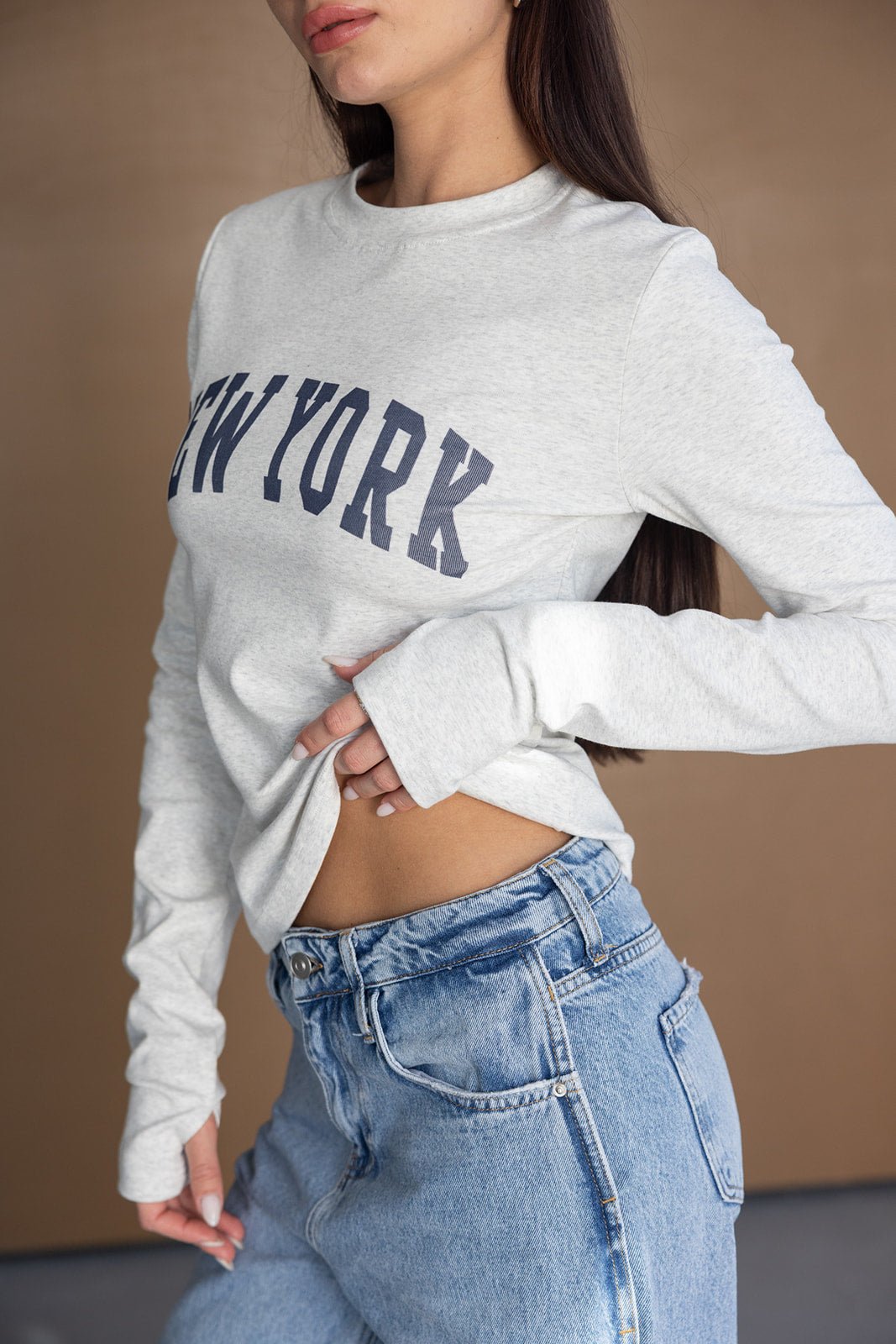 דוגמנית לובשת חולצת שרוולים אפורה עם הדפס ניו יורק ומכנסי ג'ינס אופנתיים לנשים