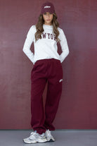 אופנה לנשים: דוגמנית לובשת חולצת ניו יורק לבנה, מכנסי טרנינג בורדו, כובע תואם ונעלי סניקרס