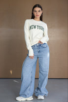 דוגמנית לובשת חולצה לבנה עם כיתוב NEW YORK, ג'ינס רחב ונעלי סניקרס אופנתיות, אופנה לנשים צעירות