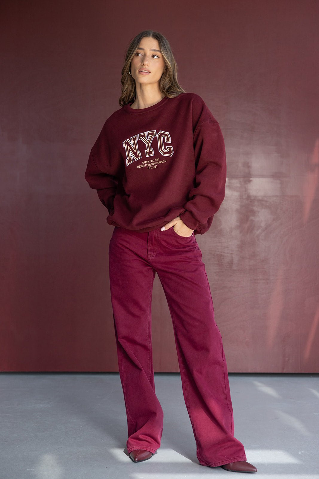 אישה צעירה לובשת סווטשירט בורדו עם הדפס NYC ומכנסיים רחבים בורדו, אופנה לנשים