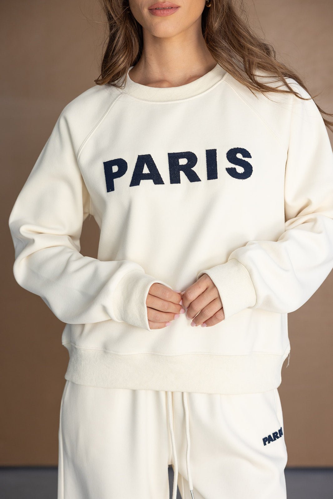 דוגמנית לובשת סט קז'ואל לנשים בצבע שמנת עם כיתוב PARIS על הסווטשירט והמכנסיים