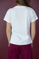 אישה לובשת חולצת טי לבנה ומכנסיים בורדו, צילום מגב על רקע אדום, אופנת נשים ונערות