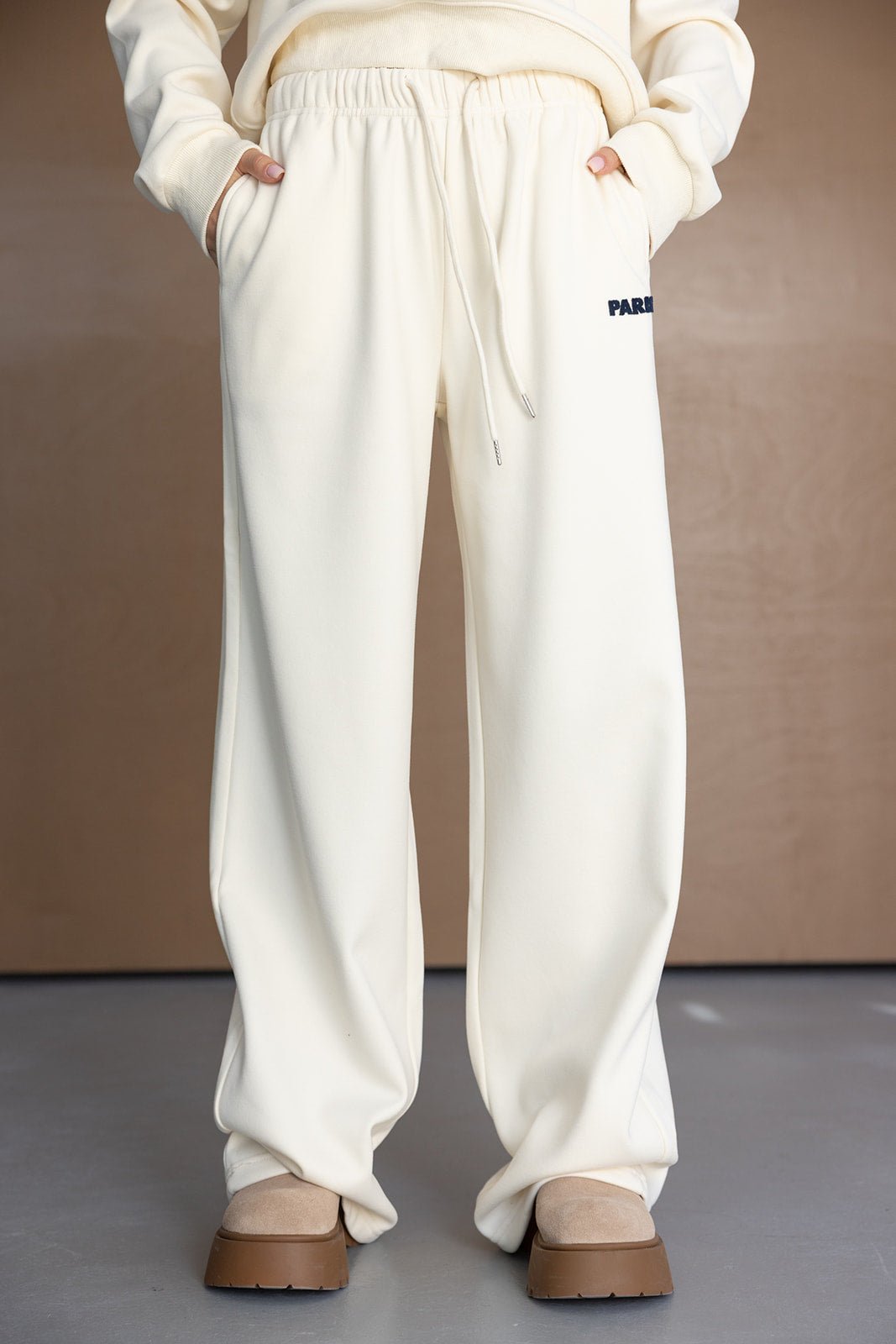 מכנסי טרנינג נשים בגזרת בוי פרנד בצבע שמנת, מותן עם גומי ושרוך, כיסים, רקמת לוגו קטנה