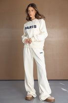 דוגמנית לובשת סט טרנינג לבן לנשים עם הדפס PARIS, רקע חום, אופנת נשים צעירה