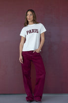 דוגמנית לובשת טי שירט לבנה עם כיתוב PARIS ומכנסיים בורדו רחבים, אופנת נשים צעירה