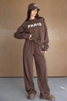 דוגמנית לובשת סט טרנינג חום לנשים עם כיתוב PARIS, כולל כובע וטוטאל לוק אופנתי.