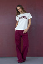 אישה עם חולצת טי לבנה הדפס PARIS ומכנסי ג'ינס בורדו, אופנת קז'ואל לנשים