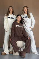 שלוש דוגמניות לבושות בטרנינג אופנתי עם כיתוב PARIS בצבעים חום, שמנת ואפור, אופנת נשים חורף