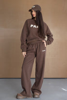 אישה לובשת סט טרנינג חום אופנתי עם כיתוב PARIS, כובע תואם ונעליים שטוחות