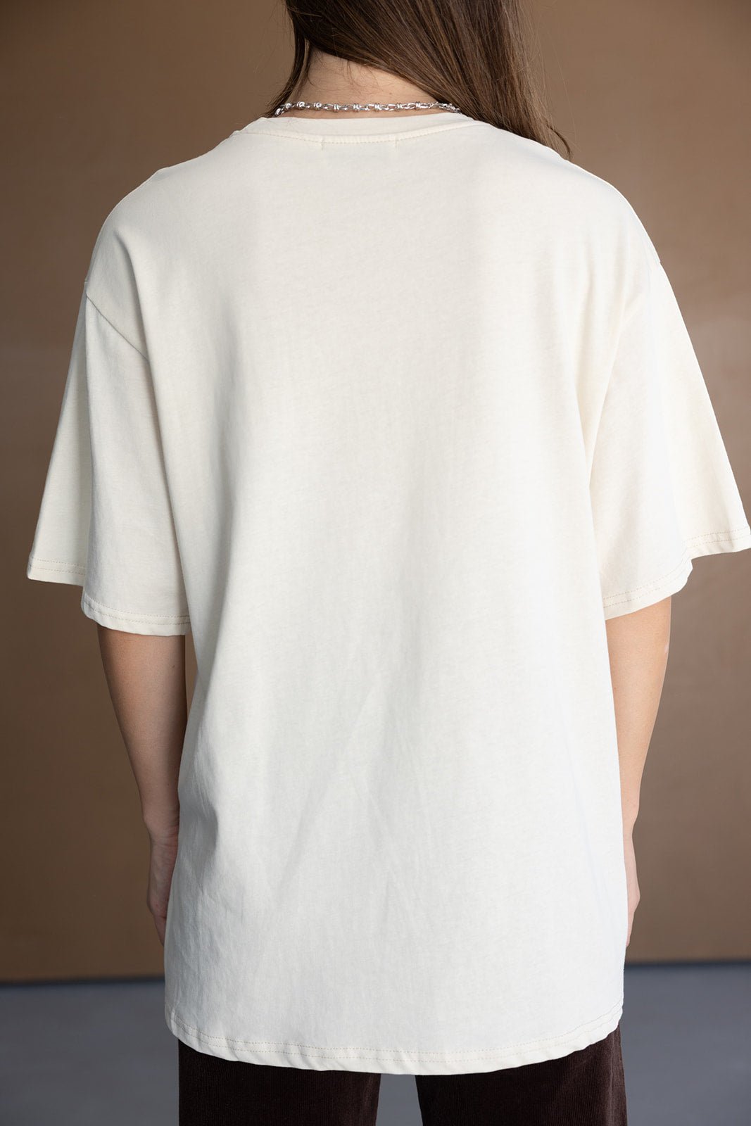חולצת טי שירט רחבה לנשים בצבע אוף וויט, מבד כותנה, מצולמת מאחור על דוגמנית