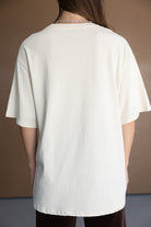 חולצת טי שירט רחבה לנשים בצבע אוף וויט, מבד כותנה, מצולמת מאחור על דוגמנית