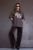 אישה לובשת חולצת טי שוקולד עם הדפס ואותיות, מכנסי קטיפה חומים, משקפי שמש אופנתיות