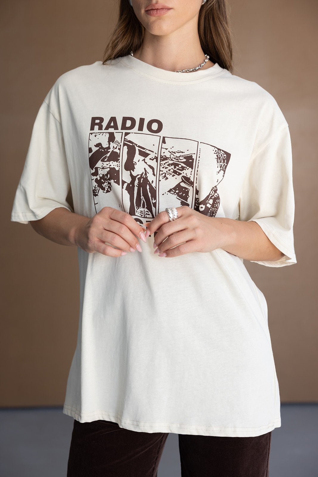 אישה לובשת חולצת טי שירט אופנתית בצבע שמנת עם הדפס גרפי ומילה RADIO, בסגנון קז'ואל לנשים