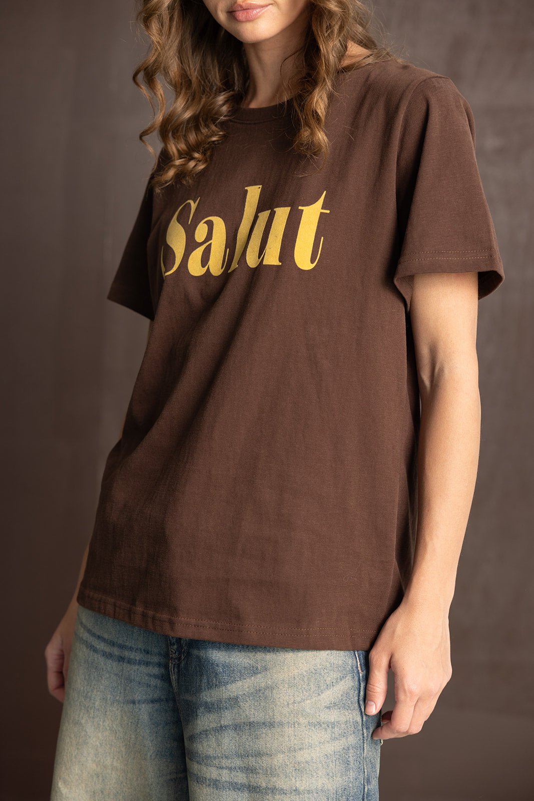 חולצת טי שירט חומה עם כיתוב Salut בזהב, משולבת עם ג'ינס בהיר לאישה