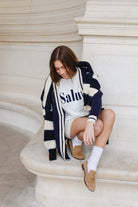 נערה יושבת בלבוש אופנתי, קרדיגן פסים כחול-לבן, חולצת טי ושורט לבן, מוקסינים חומים