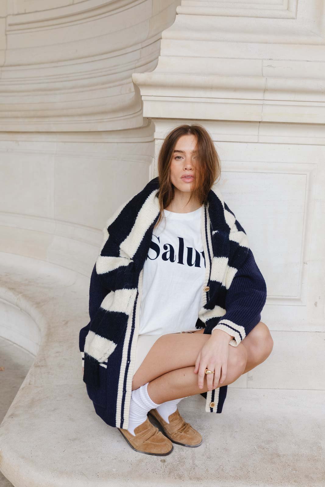 אופנת נשים צעירה, דוגמנית יושבת עם סוודר עבה בצבע שחור-לבן, חולצת טי לבנה ומוקסינים חומים