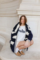 אופנת נשים צעירה, דוגמנית יושבת עם סוודר עבה בצבע שחור-לבן, חולצת טי לבנה ומוקסינים חומים