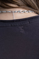 תקריב על גב חולצת נשים כהה עם רקמת אות S ושרשרת כסף עבה, אופנה טרנדית לצעירות