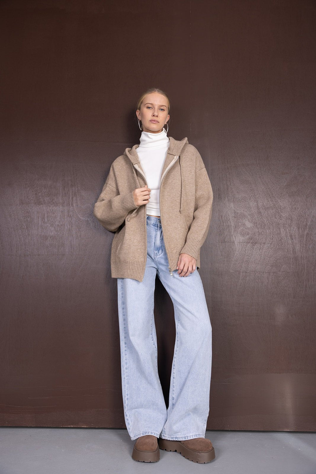 אישה לובשת סוודר חום בשילוב מכנסי ג'ינס רחבים ונעלי פלטפורמה, מראה אופנתי חורפי