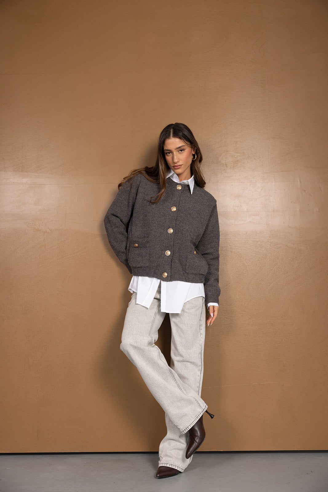 אישה לובשת סוודר אפור מכופתר, חולצה לבנה ומכנסי ג'ינס רחבים, לוק אופנתי חורפי