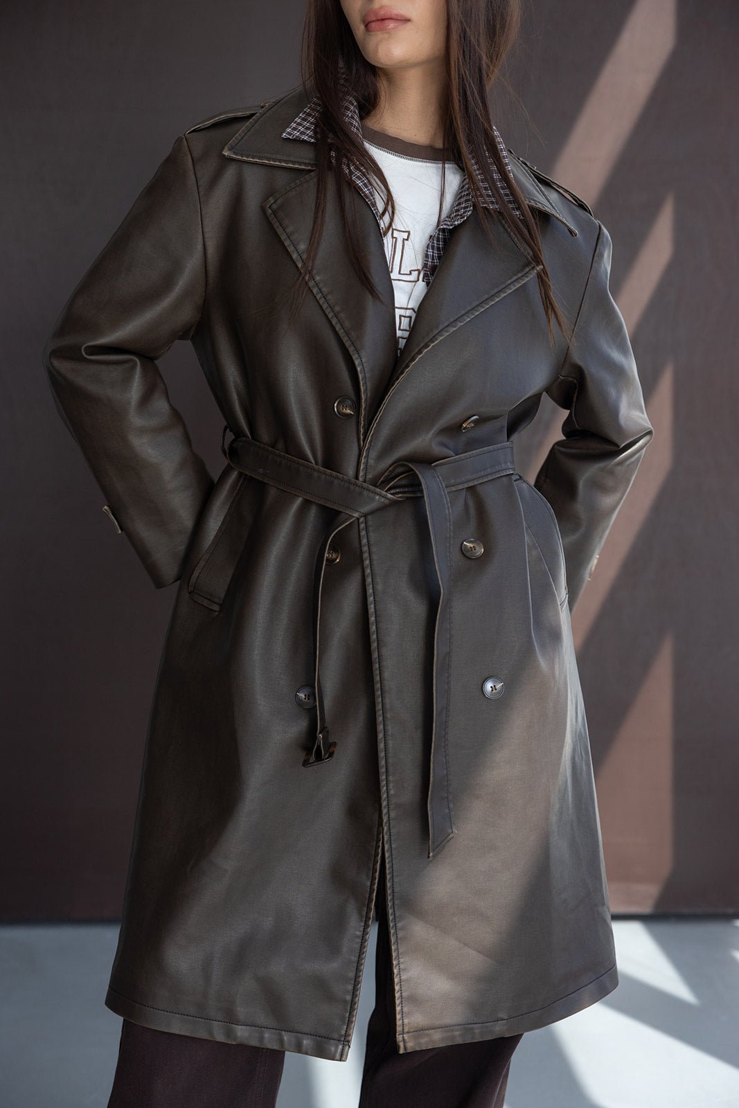 אישה לובשת מעיל טרנץ' עור אופנתי בצבע כהה, עם חגורה וכפתורים, בסגנון חורף לנשים.