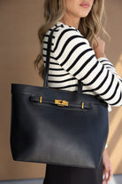 אישה עם סוודר פסים מחזיקה תיק צד גדול עור שחור עם אבזם זהב, אופנת נשים אלגנטית