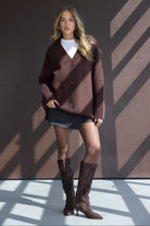 דוגמנית לובשת קרדיגן חום, חצאית קצרה ומגפיים חומים, אופנת נשים צעירה לחורף