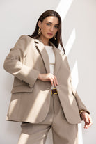 אישה לובשת חליפת מכנסיים בגוון בז', חולצה לבנה ועגילים זהובים, מבט אופנתי קלאסי לנשים