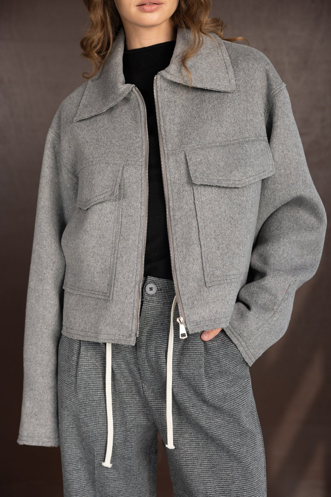 אישה לובשת ז'קט אפור עם רוכסן וכיסים, מכנסי משבצות עם שרוך, אופנת חורף לנשים