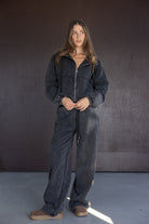 אישה צעירה לובשת סט בגדי פנאי ספורטיבי בצבע אפור כהה עם רוכסן, על רקע נייטרלי, אופנת נשים עדכנית