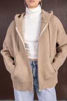 אישה לובשת קפוצ'ון צמר בז' עם רוכסן, טופ גולף לבן וג'ינס כחול בהיר, אופנה טרנדית לנשים