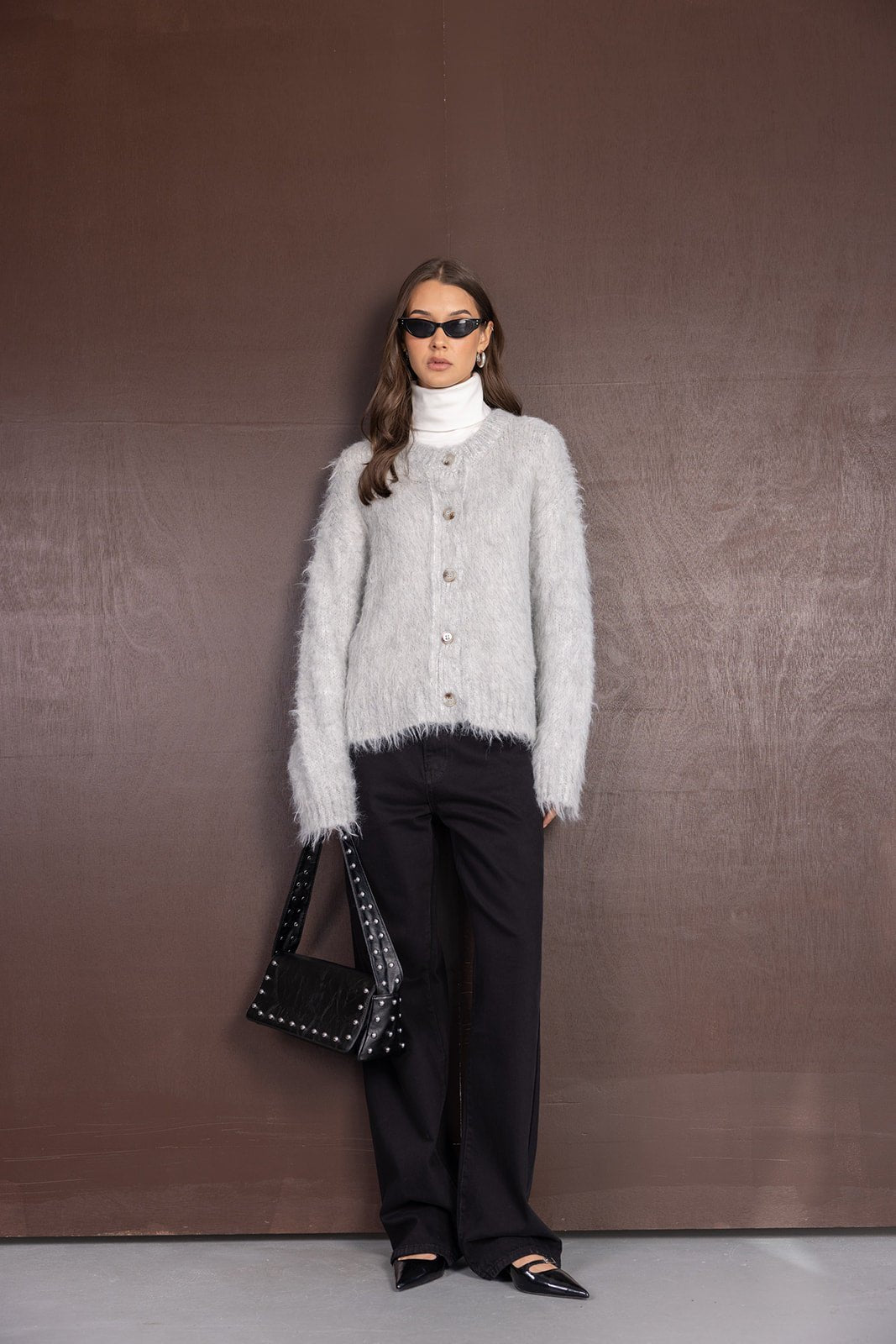 דוגמנית בג׳ינס שחורים, סוודר פרוותי אפור, גולף לבן, תיק שחור ומשקפי שמש, אופנת חורף לנשים