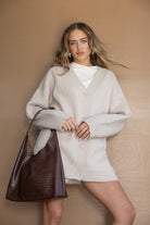 אישה לובשת קרדיגן סרוג בז' עם כפתורים, חולצה לבנה ותיק צד חום טרנדי, אופנה לנשים