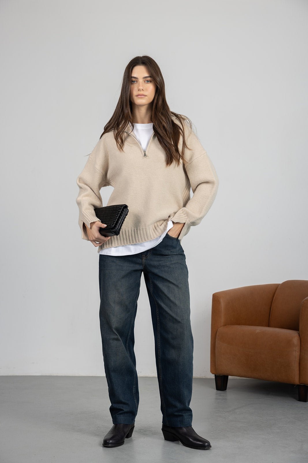 דוגמנית לובשת סוודר בז' עם רוכסן, ג'ינס רחב ומחזיקה תיק קלאץ' שחור, סטייל קז'ואל לנשים