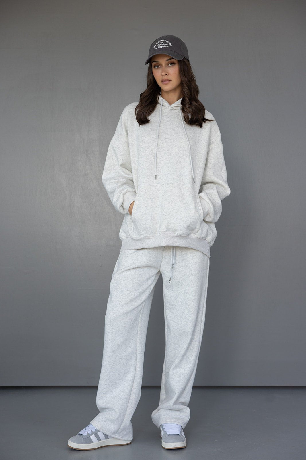 דוגמנית לובשת סט טרנינג אפור לנשים, סווטשירט ומכנסיים רחבים, כובע ונעלי סניקרס