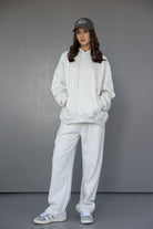 דוגמנית לובשת סט טרנינג אפור לנשים, סווטשירט ומכנסיים רחבים, כובע ונעלי סניקרס