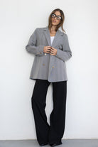 דוגמנית לובשת בלייזר אפור מחויט עם כפתורים זהובים, מכנסיים שחורים רחבים ומשקפי אופנה