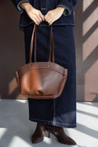 תיק נשי חום מעור עם ידיות ארוכות, לבוש ג'ינס ומגפונים חומים, אופנה לנשים