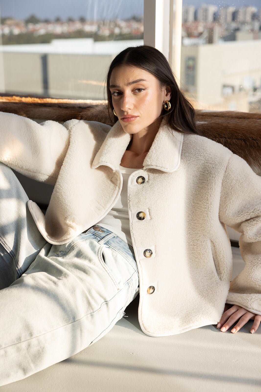 דוגמנית לובשת מעיל בוקלה אופנתי בצבע שמנת ומכנסי ג'ינס בהירים, צילום אופנה חורף