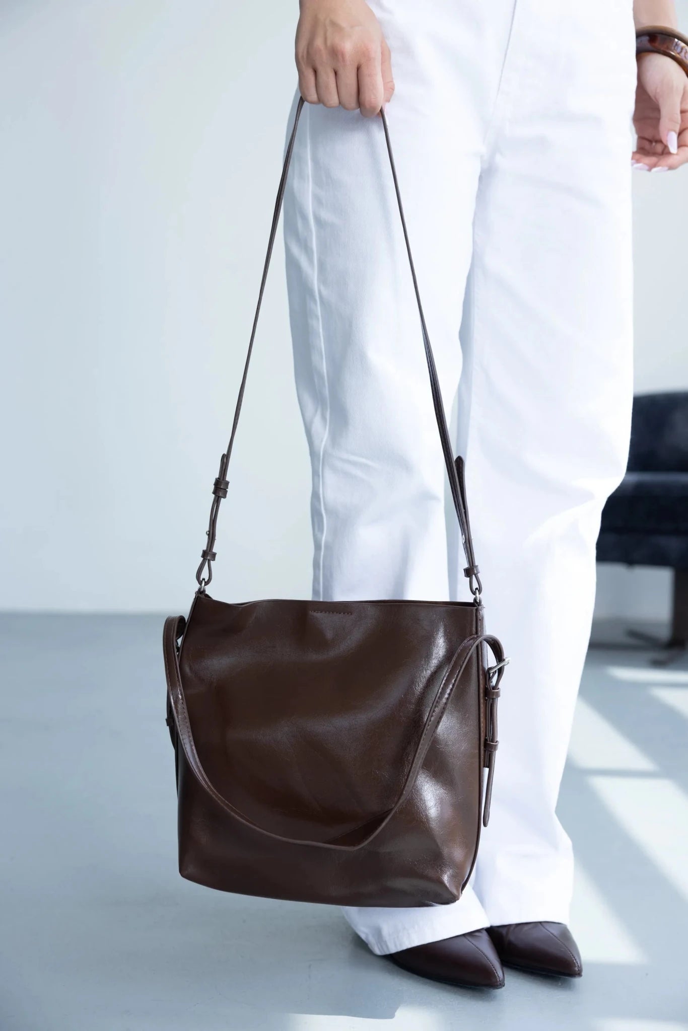 תיק צד חום מעור בסגנון קלאסי לאישה, משולב עם מכנסי בד לבנים ונעלי שפיץ אופנתיות