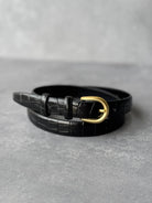 חגורת נשים שחורה עם אבזם זהב, דוגמת קרוקו, מונחת על רקע אפור