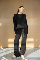 אישה לובשת סט טרנינג שחור אופנתי לנשים, חולצה ארוכה ומכנסיים רחבים, נעלי פלטפורמה בז'.