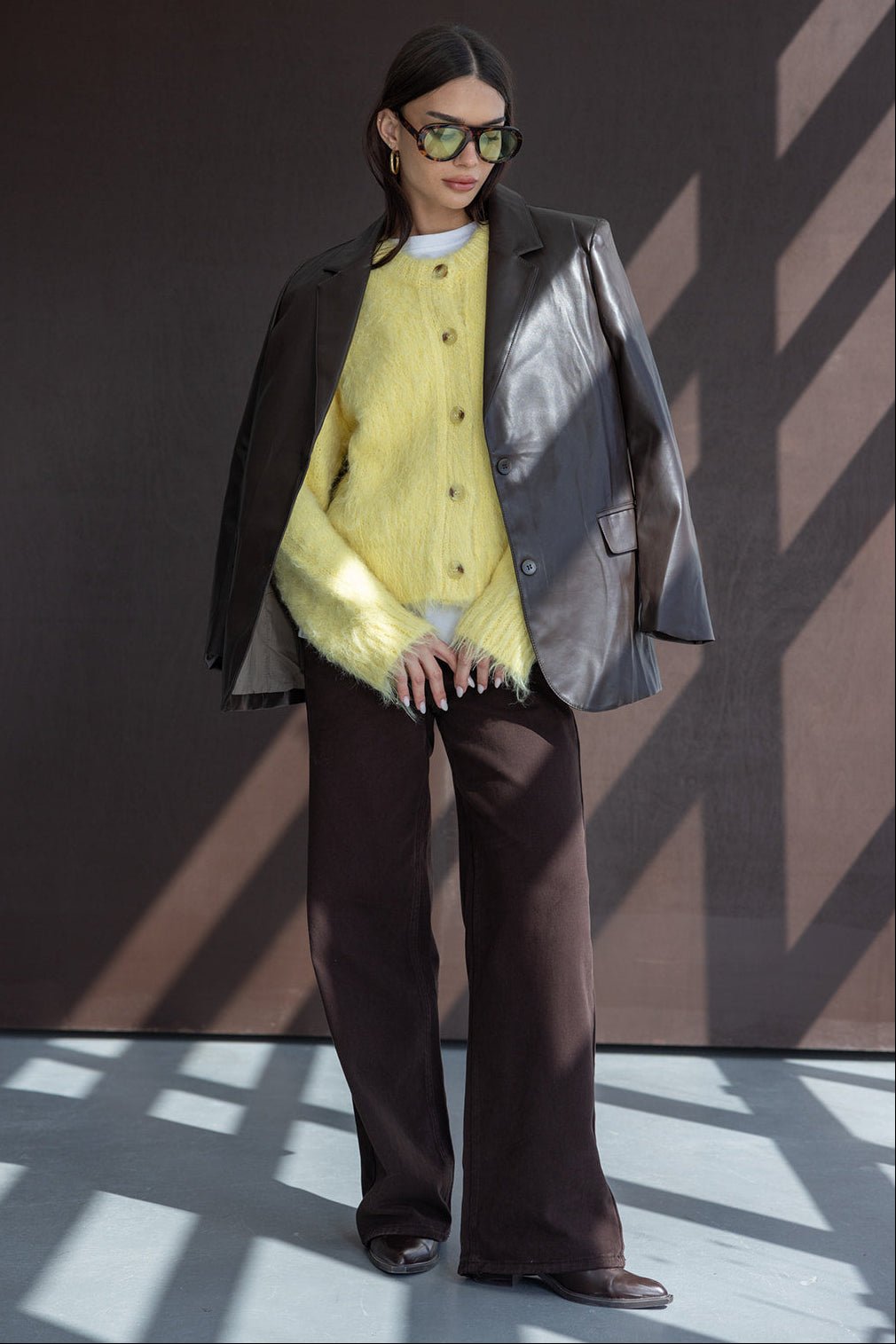 אישה עם משקפי שמש, קרדיגן צהוב פלאפי, בלייזר עור כהה ומכנסיים רחבים, לוק אופנתי לנשים